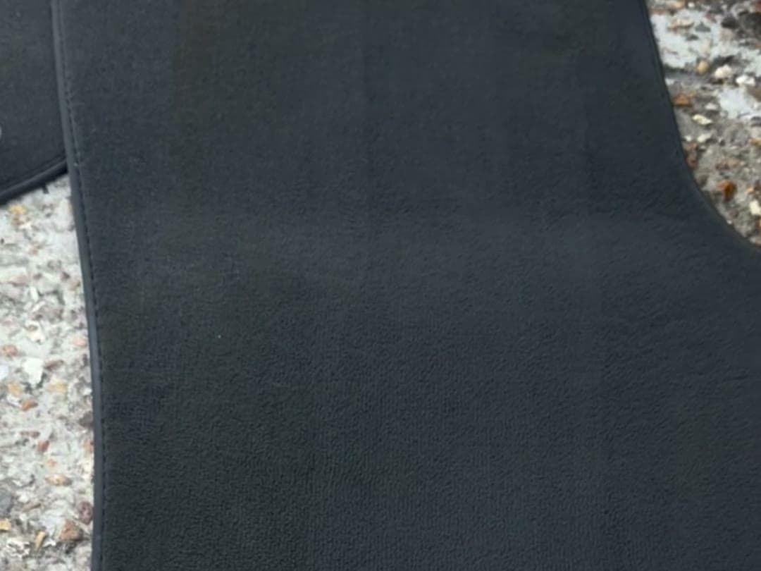 Tapis de sol de voiture noir après nettoyage, posé sur du gravier : bandes de passage verticales de la buse, bords du tapis visibles